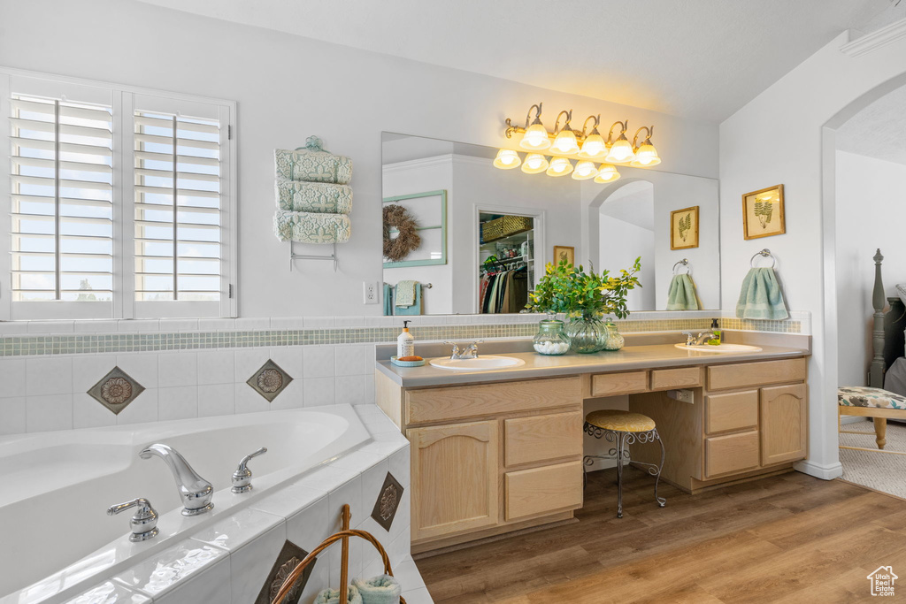 Full bathroom with double vanity, a sink, a bath, and wood finished floors