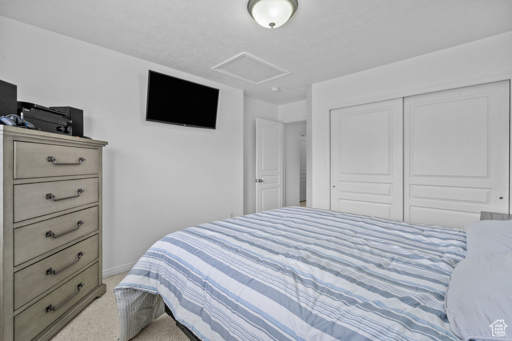 Bedroom with a closet, baseboards, attic access, and light colored carpet
