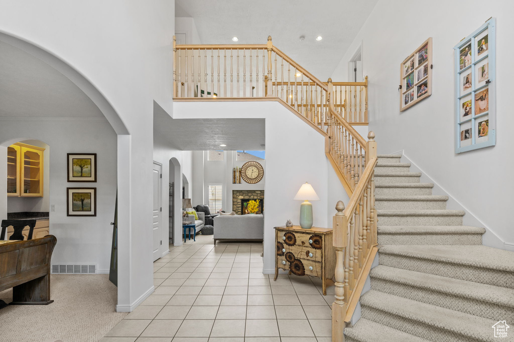Entrance foyer featuring visible vents, a towering ceiling, a fireplace, stairway, and arched walkways