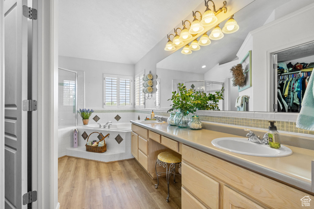 Full bath with double vanity, a shower stall, a sink, and wood finished floors
