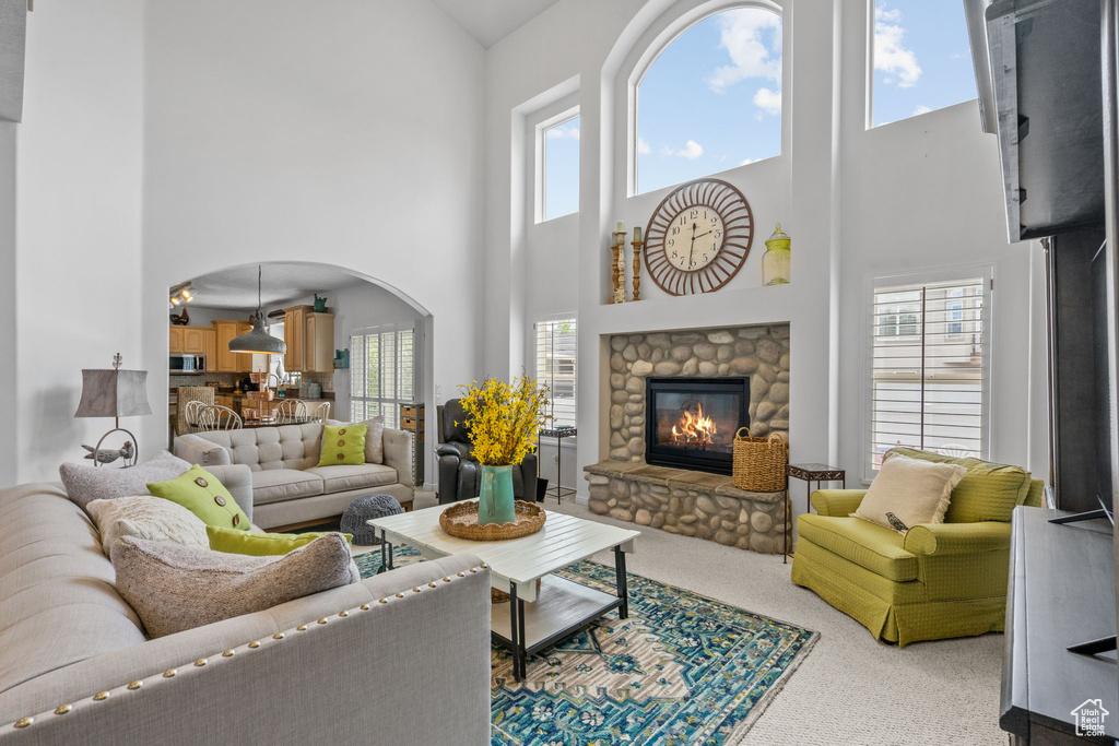 Living room featuring carpet flooring, arched walkways, a high ceiling, and a fireplace