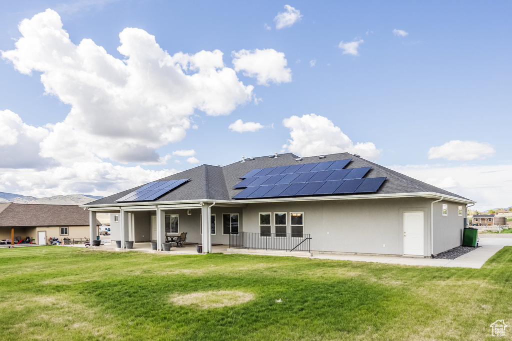 Rear view of house featuring roof mounted solar panels, a yard, and a patio area