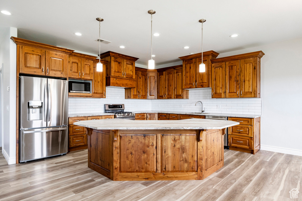 Kitchen featuring appliances with stainless steel finishes, brown cabinets, a sink, baseboards, and light wood finished floors