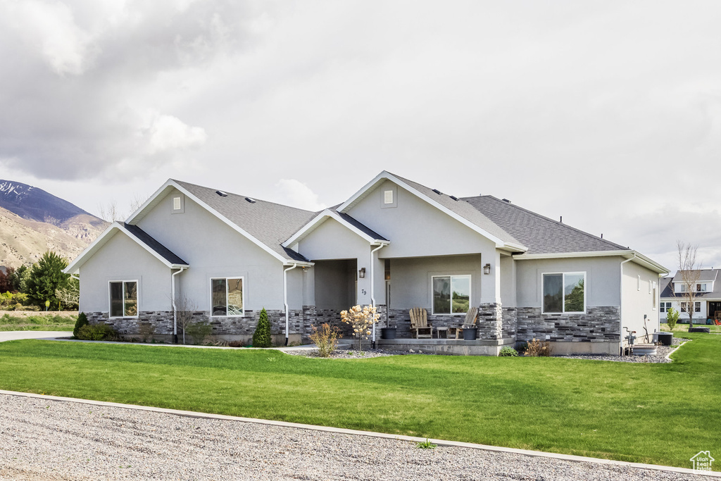 Back of property with a mountain view, stucco siding, a yard, and stone siding