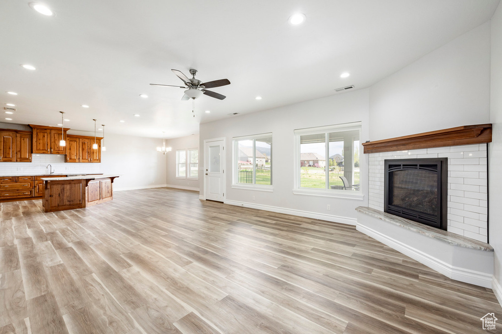 Unfurnished living room with ceiling fan with notable chandelier, baseboards, a brick fireplace, and recessed lighting