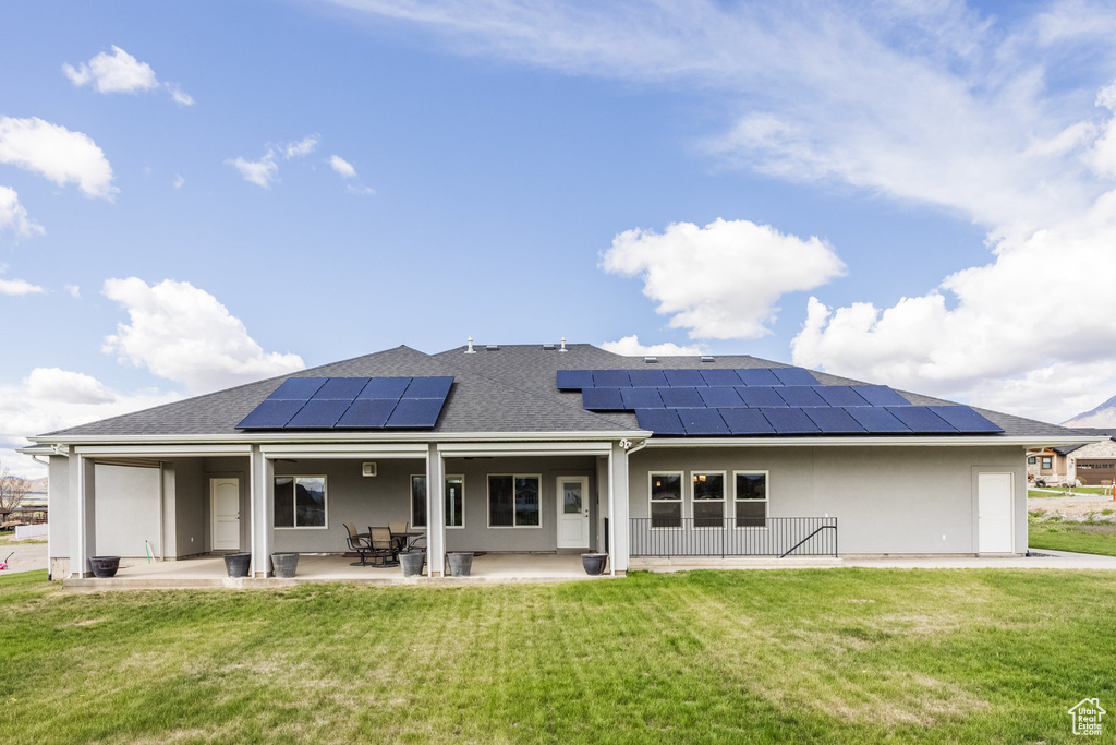 Back of property with a lawn, solar panels, a shingled roof, and a patio area