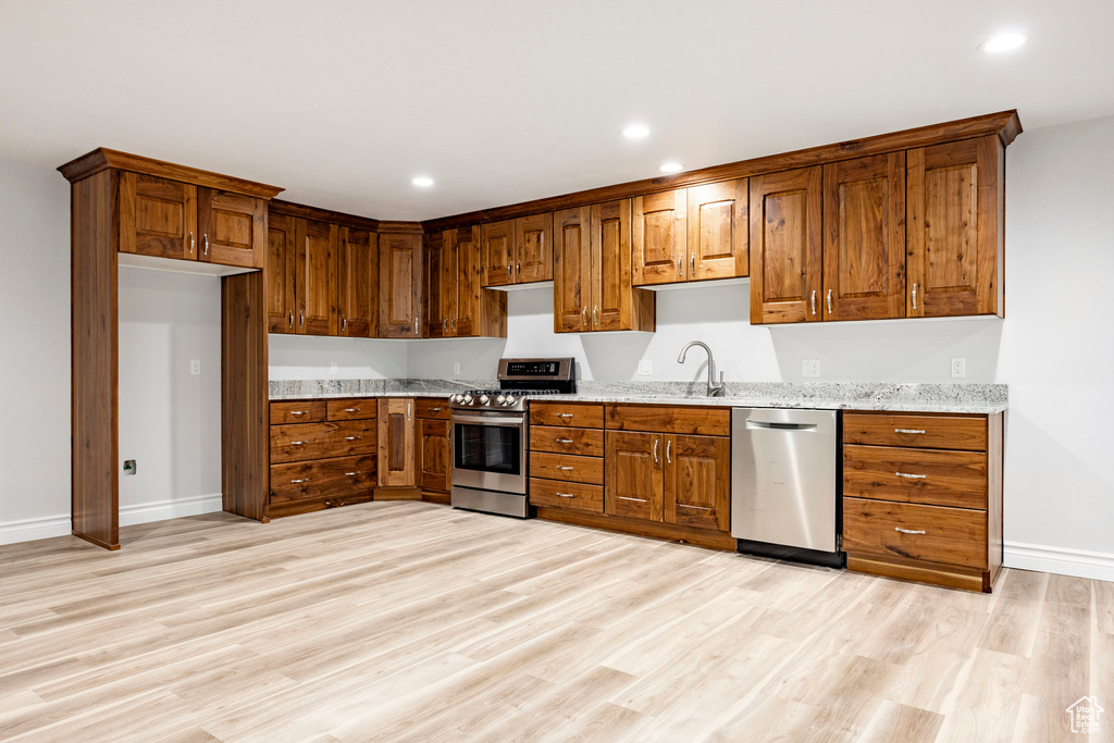 Kitchen featuring brown cabinetry, appliances with stainless steel finishes, light wood-type flooring, a sink, and baseboards