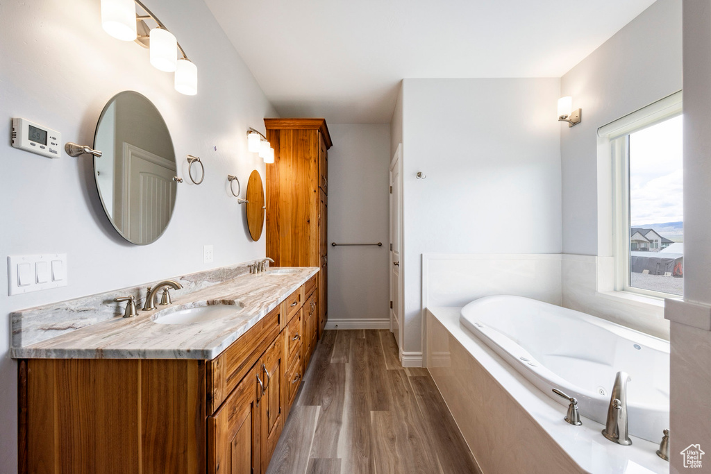 Full bath featuring double vanity, a sink, a bath, and wood finished floors