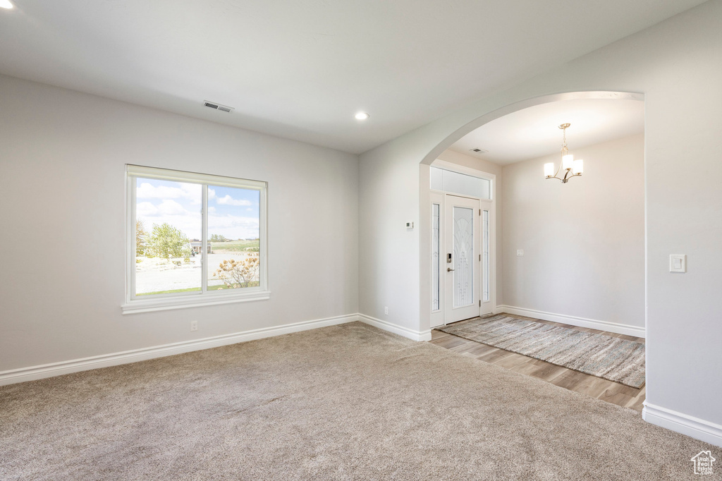 Unfurnished room with light colored carpet, visible vents, arched walkways, baseboards, and a chandelier
