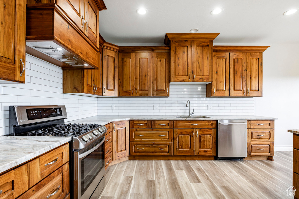 Kitchen featuring brown cabinets, a sink, light wood-style flooring, premium range hood, and stainless steel appliances