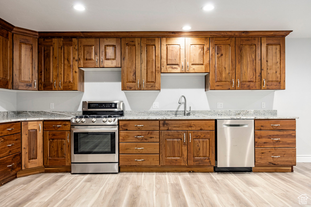 Kitchen featuring light stone countertops, light wood-type flooring, brown cabinets, a sink, and stainless steel appliances