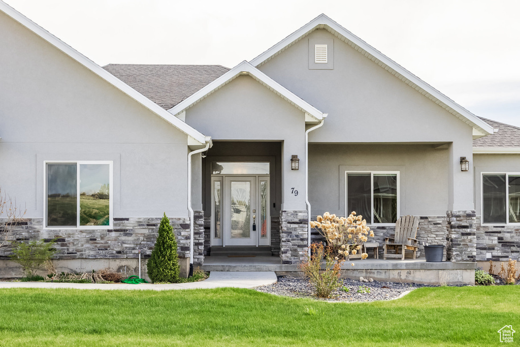 Property entrance featuring a lawn, roof with shingles, stucco siding, and stone siding