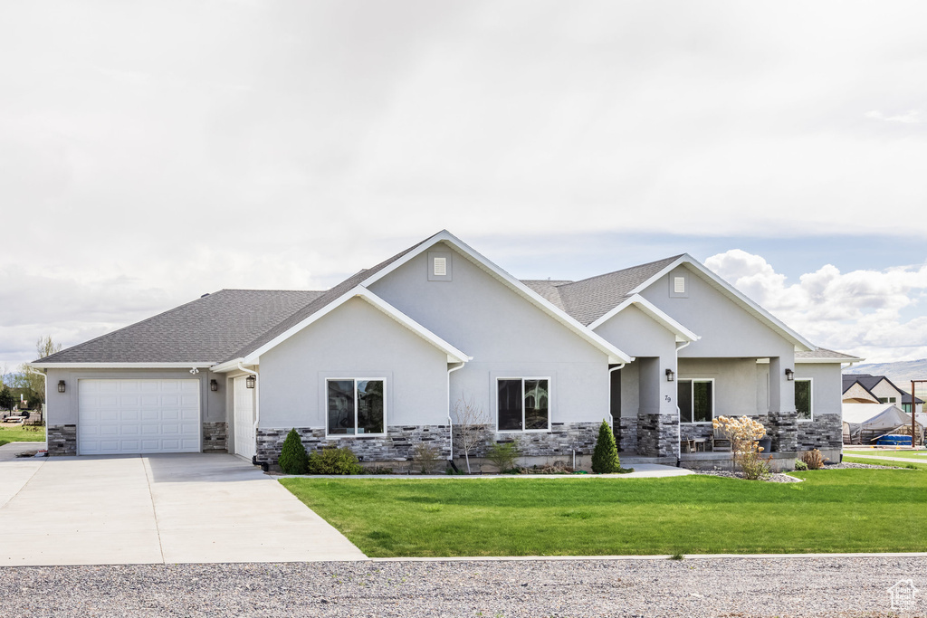 View of front of house featuring an attached garage, a front lawn, stone siding, stucco siding, and driveway