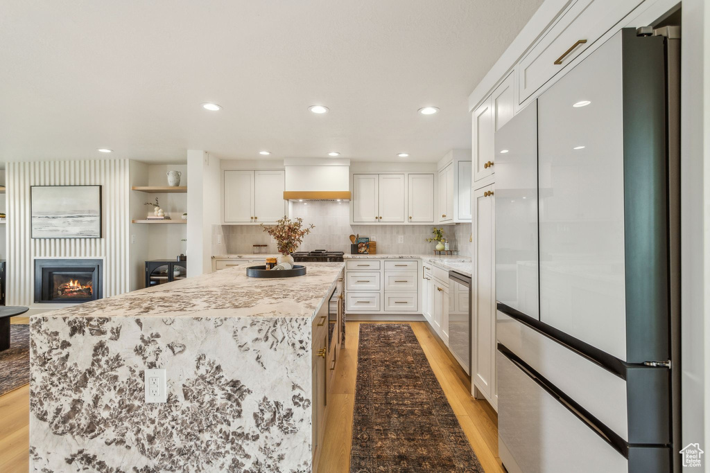 Kitchen featuring light wood-style floors, built in refrigerator, premium range hood, and a center island