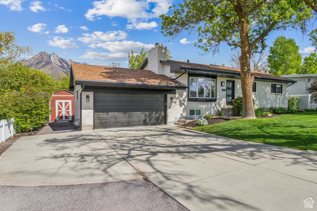 Ranch-style home with a garage, a shed, a front yard, a chimney, and concrete driveway