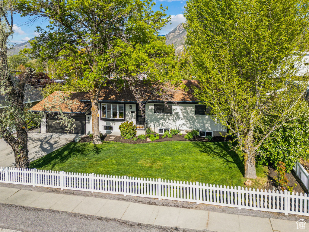 View of front facade featuring a fenced front yard, a mountain view, a front lawn, concrete driveway, and an attached garage