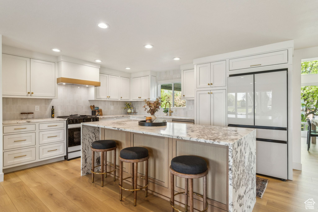 Kitchen with a breakfast bar area, a kitchen island, tasteful backsplash, light wood finished floors, and range with gas stovetop