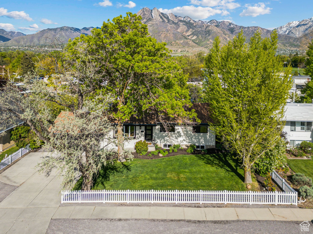 View of front of property featuring driveway, a fenced front yard, a mountain view, and a front lawn