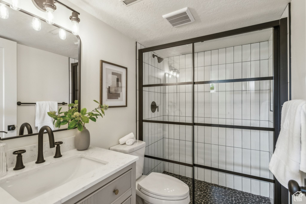 Full bathroom featuring vanity, toilet, a textured ceiling, visible vents, and tiled shower