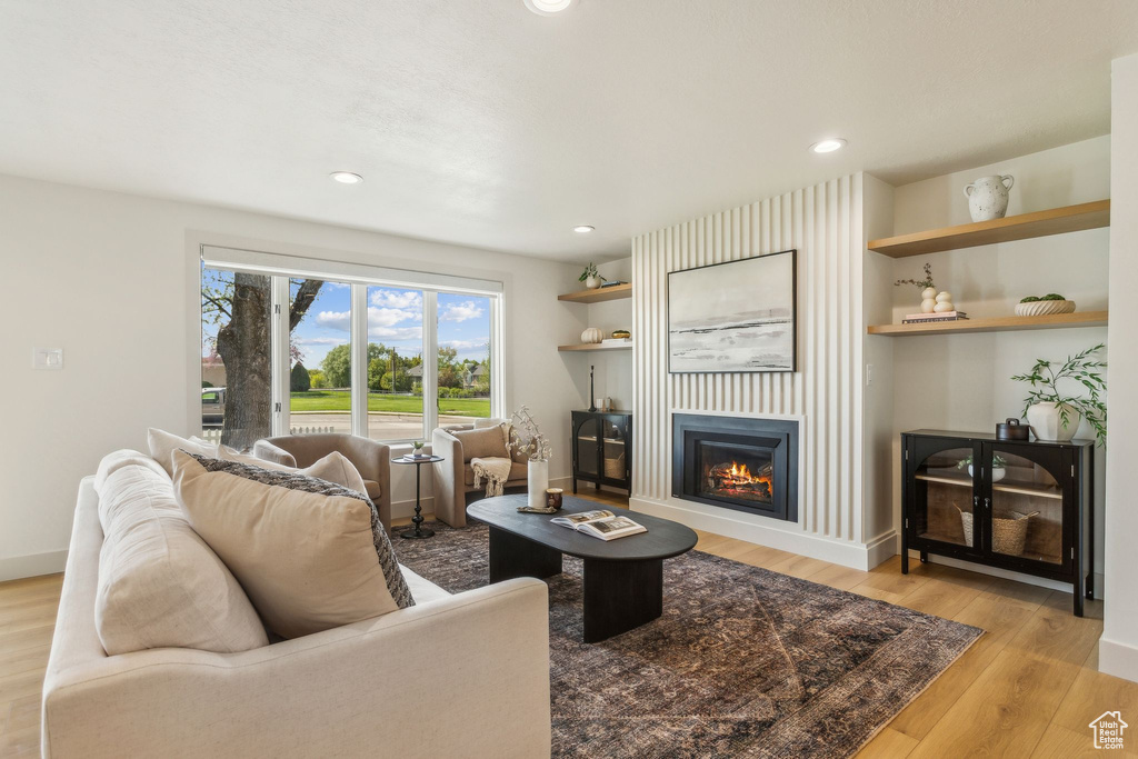 Living room featuring recessed lighting, light wood-style flooring, a glass covered fireplace, and baseboards