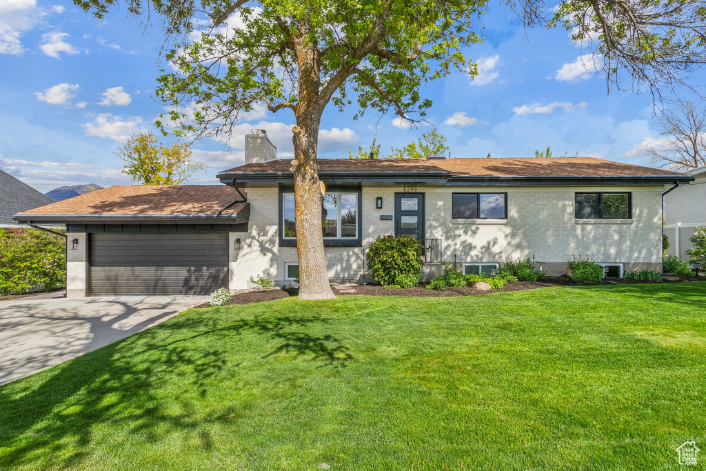 Ranch-style home featuring an attached garage, brick siding, a front yard, a chimney, and concrete driveway