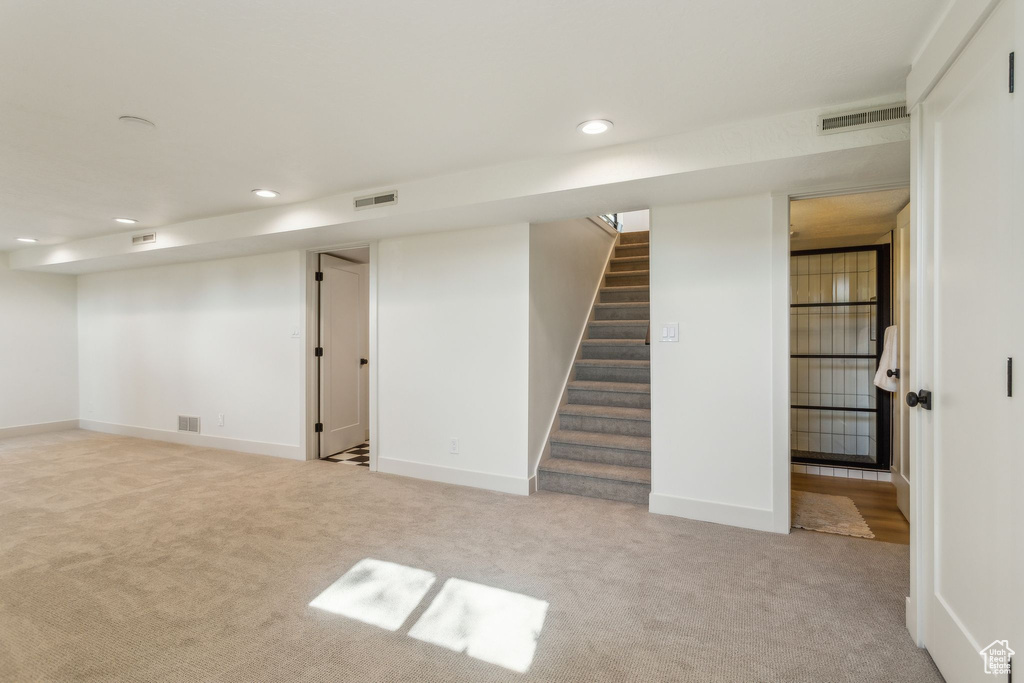 Finished below grade area featuring carpet floors, recessed lighting, visible vents, and stairway