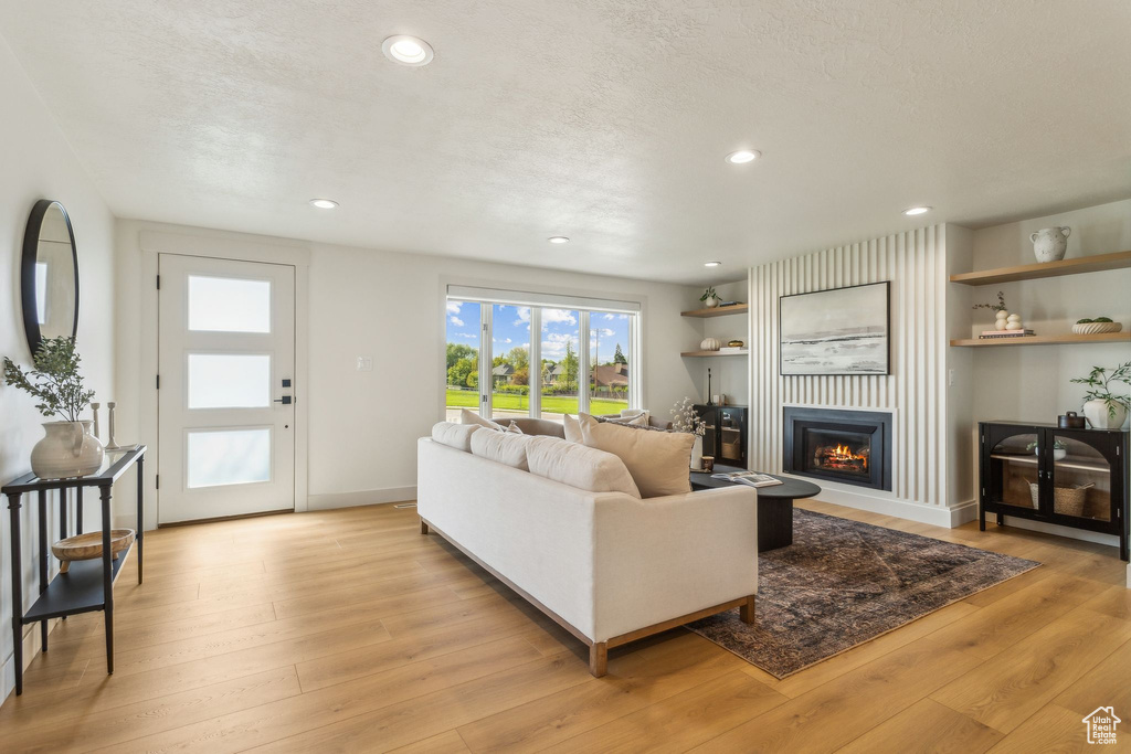 Living area featuring recessed lighting, a warm lit fireplace, and light wood finished floors