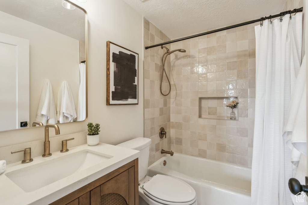 Bathroom featuring vanity, shower / bath combo, toilet, and a textured ceiling