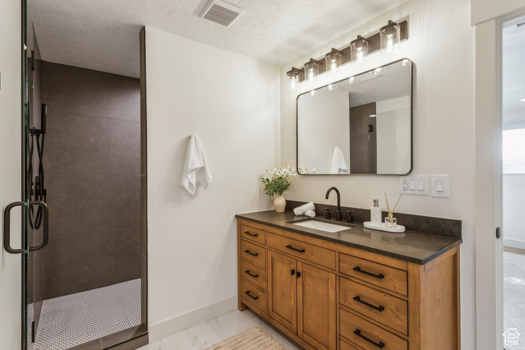 Bathroom featuring vanity, a textured ceiling, baseboards, visible vents, and a stall shower