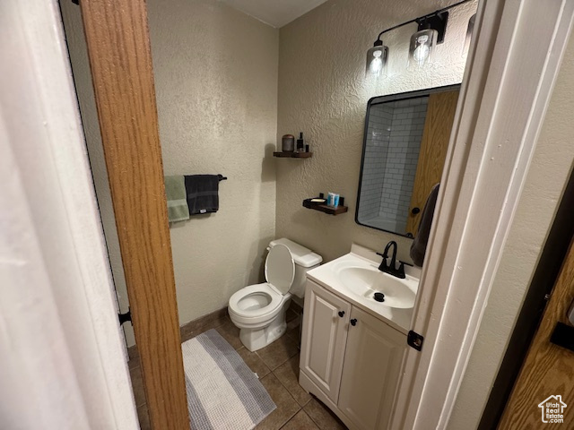 Half bath featuring tile patterned floors, baseboards, vanity, toilet, and a textured wall