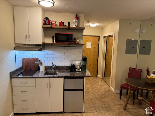 Kitchen with a sink, electric panel, under cabinet range hood, and black appliances