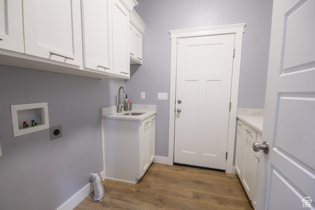 Laundry area featuring wood finished floors, hookup for a washing machine, a sink, cabinet space, and hookup for an electric dryer