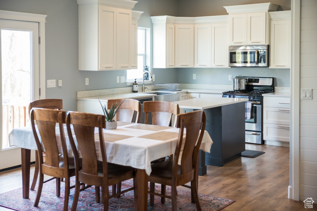 Kitchen featuring appliances with stainless steel finishes, wood finished floors, a sink, light countertops, and white cabinetry