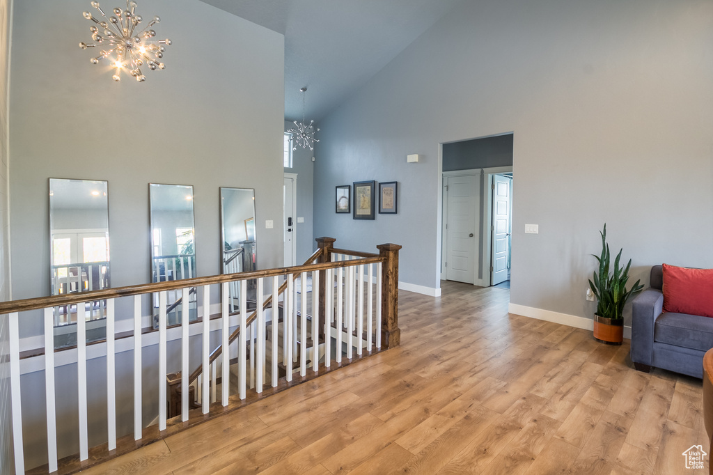 Hall featuring an inviting chandelier, high vaulted ceiling, baseboards, an upstairs landing, and wood finished floors