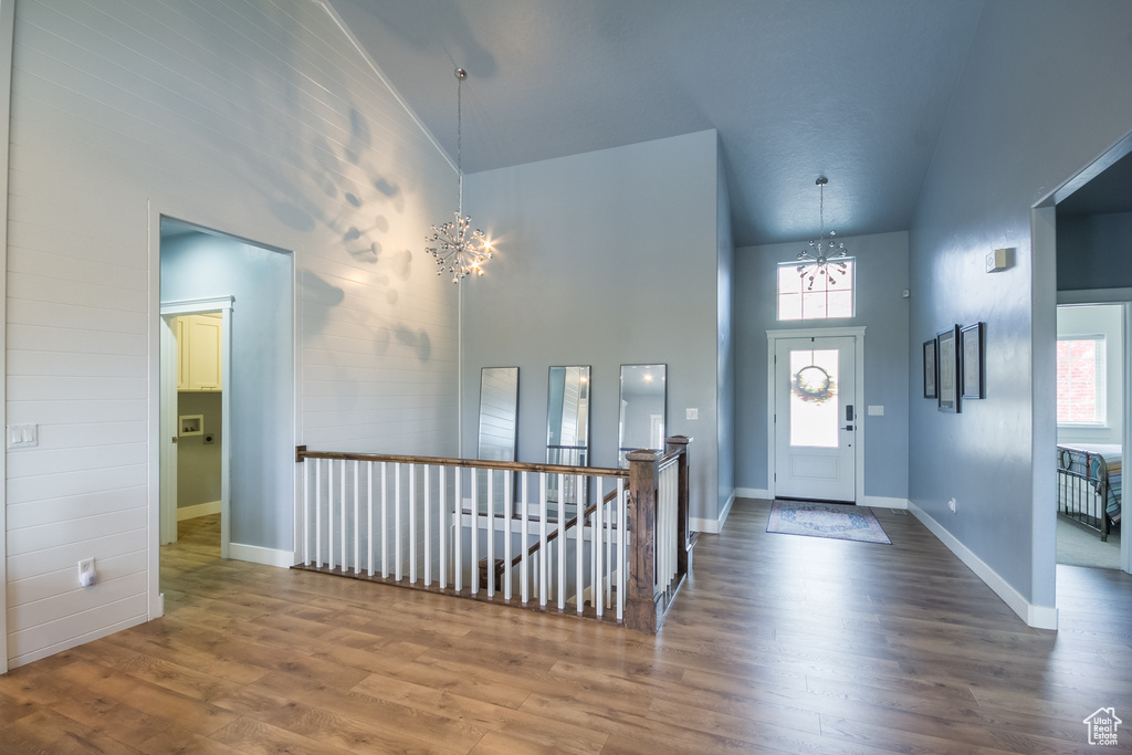 Entryway with high vaulted ceiling, an inviting chandelier, a wealth of natural light, and wood finished floors