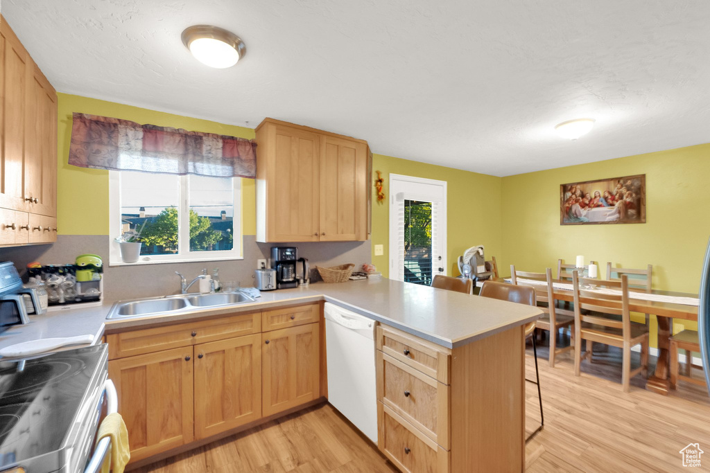 Kitchen featuring a peninsula, a breakfast bar, a sink, light wood-style flooring, and dishwasher