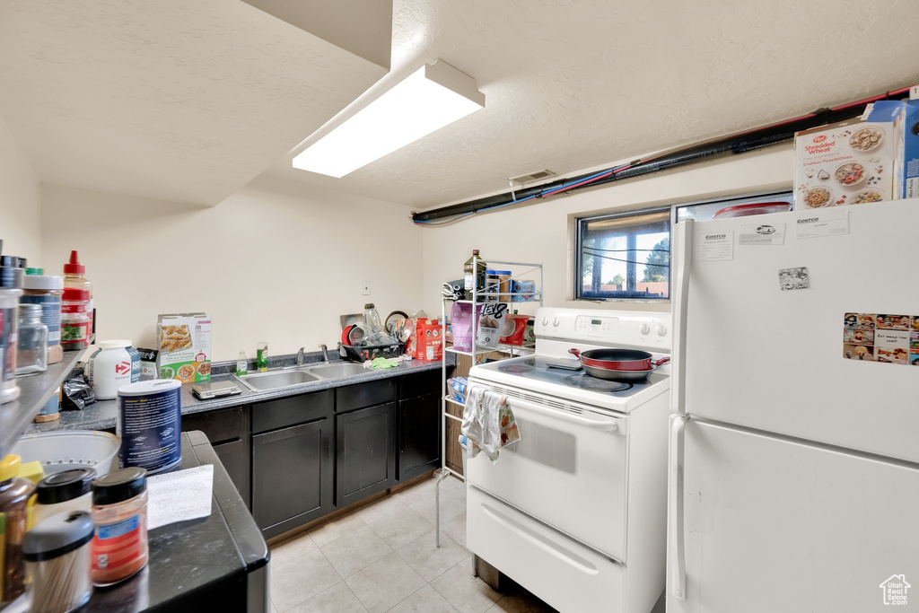 Kitchen featuring a sink, light tile patterned floors, dark cabinetry, and white appliances