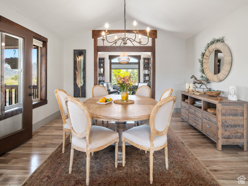 Dining room with baseboards, a chandelier, lofted ceiling, and light wood-type flooring