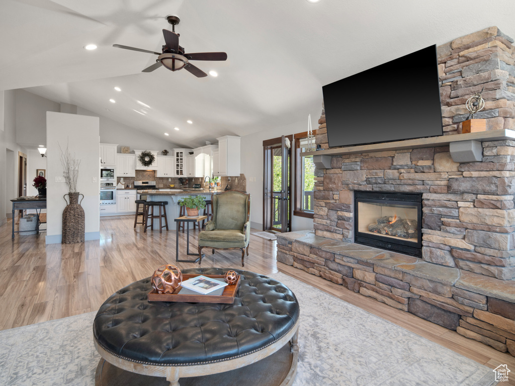 Living area featuring lofted ceiling, light wood-style floors, a stone fireplace, recessed lighting, and a ceiling fan