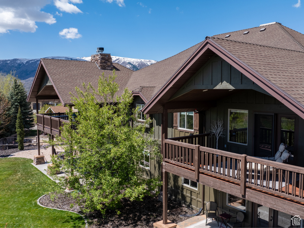 Rear view of property with roof with shingles, board and batten siding, a deck with mountain view, a chimney, and a patio area