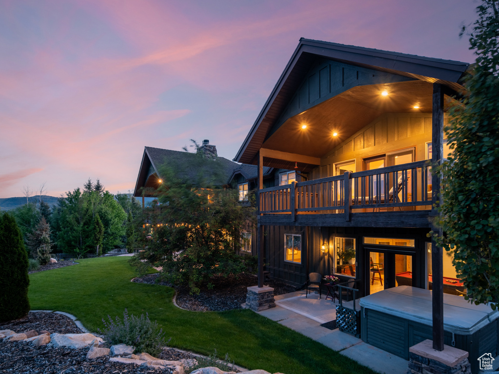 Back of house featuring board and batten siding, a lawn, a patio area, and a hot tub