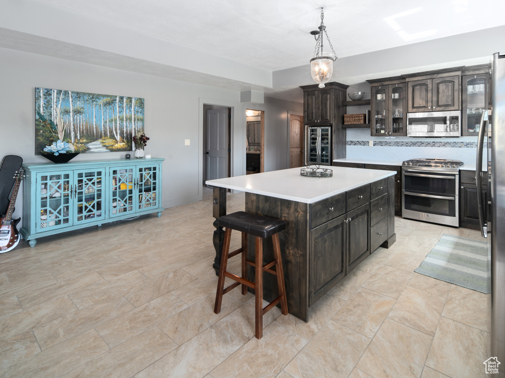 Kitchen featuring light countertops, stainless steel appliances, backsplash, a kitchen island, and glass insert cabinets
