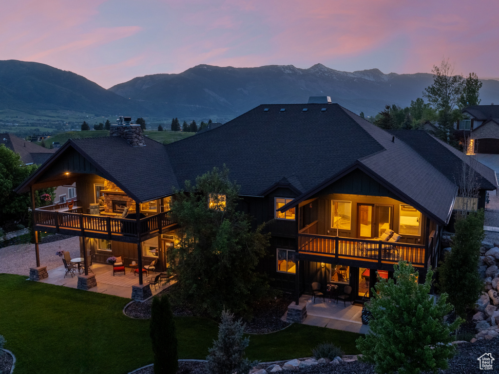 Back of property at dusk featuring a patio, roof with shingles, a mountain view, and a yard