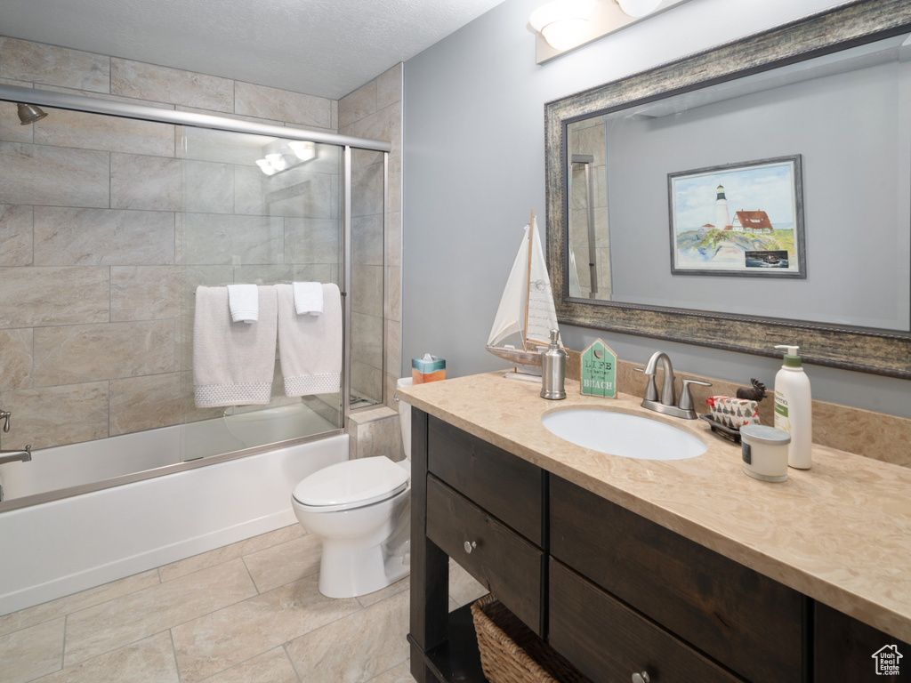Full bathroom with vanity, a textured ceiling, enclosed tub / shower combo, and toilet