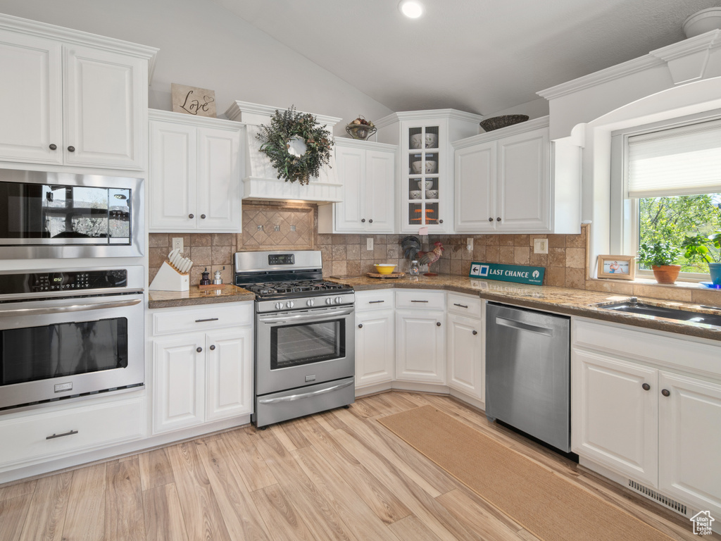 Kitchen with stainless steel appliances, visible vents, white cabinetry, and lofted ceiling