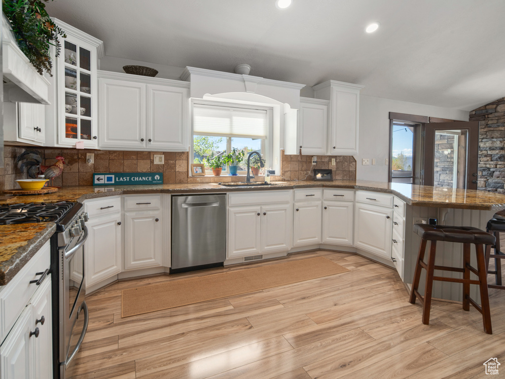 Kitchen with white cabinets, appliances with stainless steel finishes, a sink, light wood-style floors, and a peninsula
