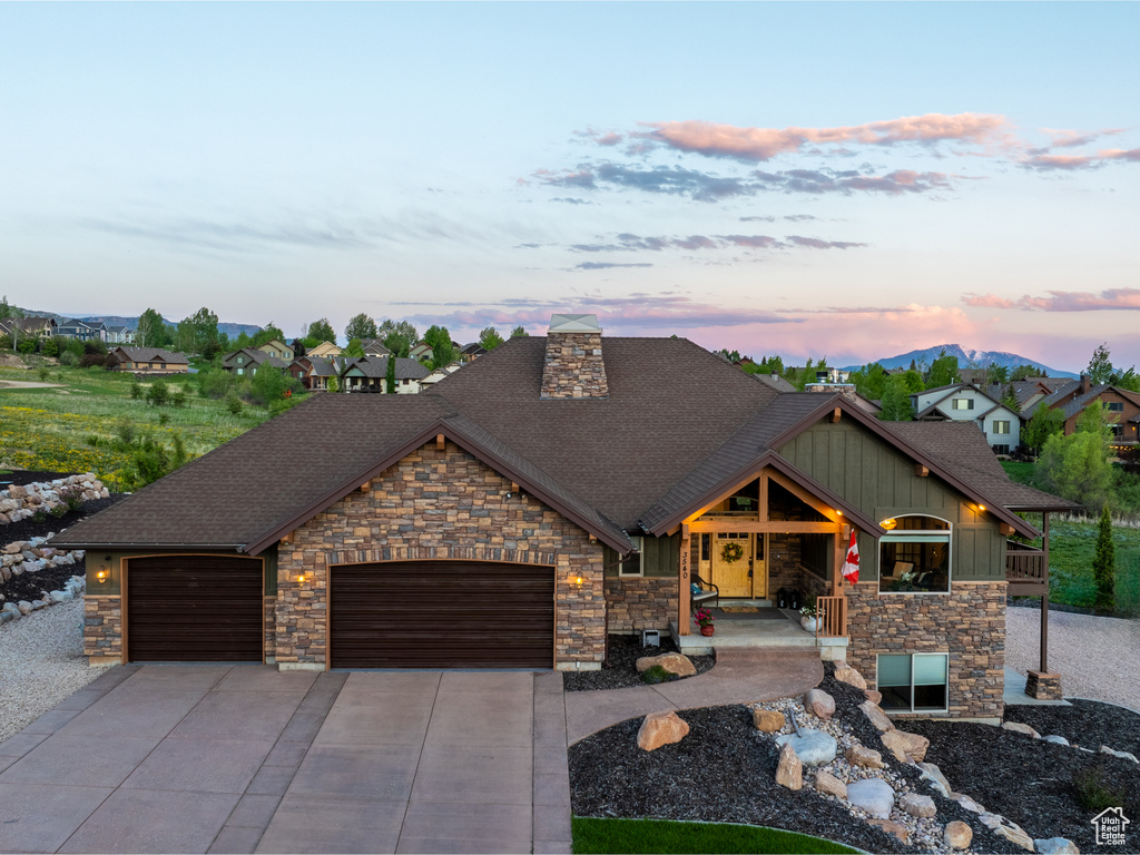 View of front of home with stone siding, an attached garage, roof with shingles, board and batten siding, and concrete driveway