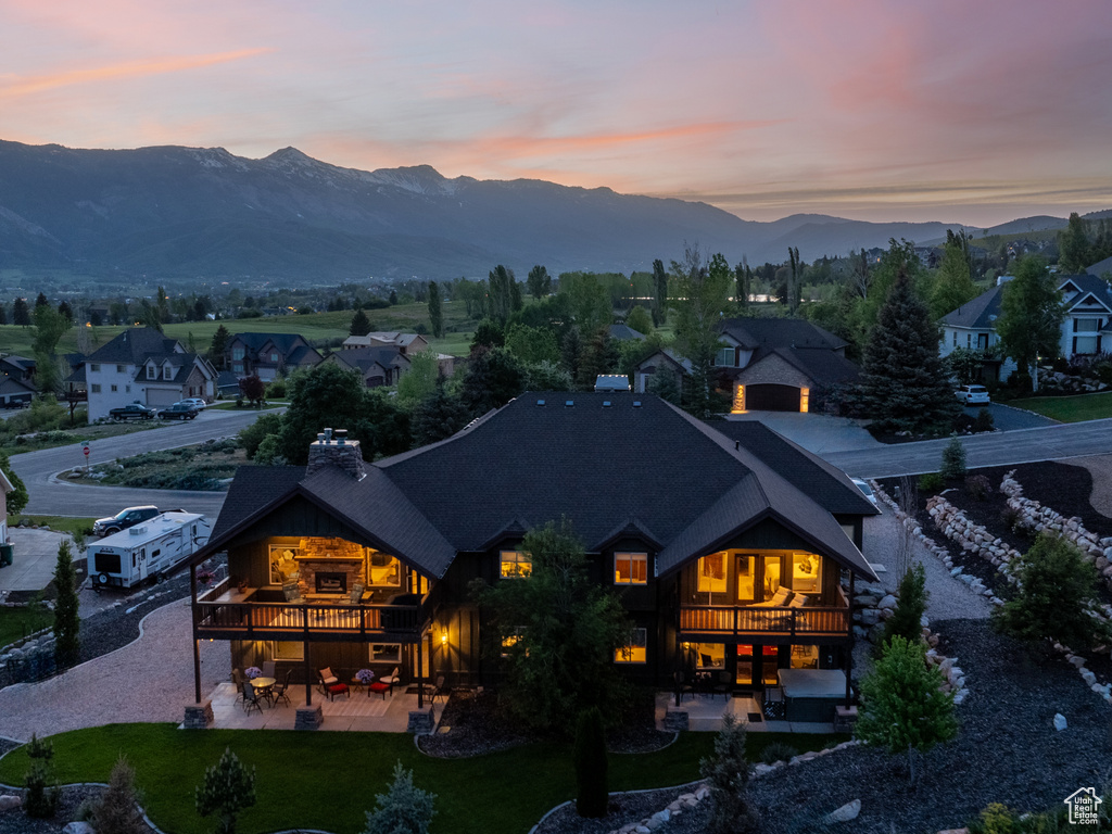 Back of house at dusk with a balcony, a patio area, a chimney, and a mountain view