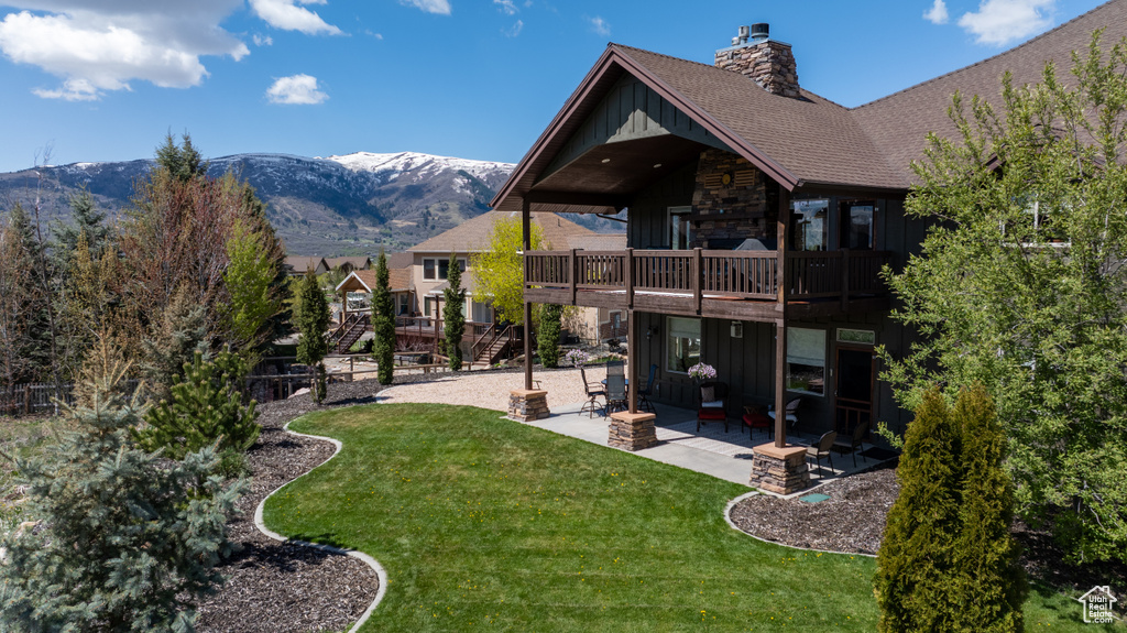 Back of property featuring board and batten siding, a chimney, a lawn, a patio, and a deck with mountain view