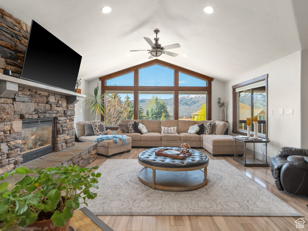 Living room with wood finished floors, a stone fireplace, ceiling fan, recessed lighting, and vaulted ceiling